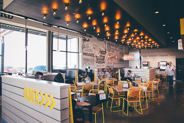 Interior of Super Chix with yellow chairs and many light bulbs attached to the ceiling. 