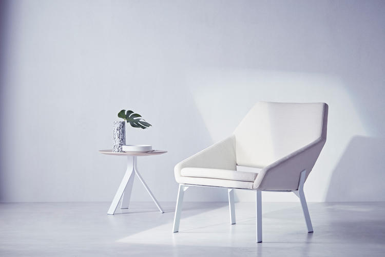 A white, modern chair next to a side table. 