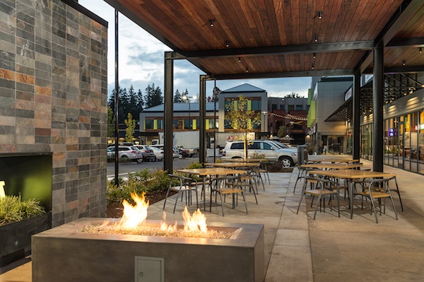 A lit fire pit next to next patio seating, with a wooden ceiling above. 
