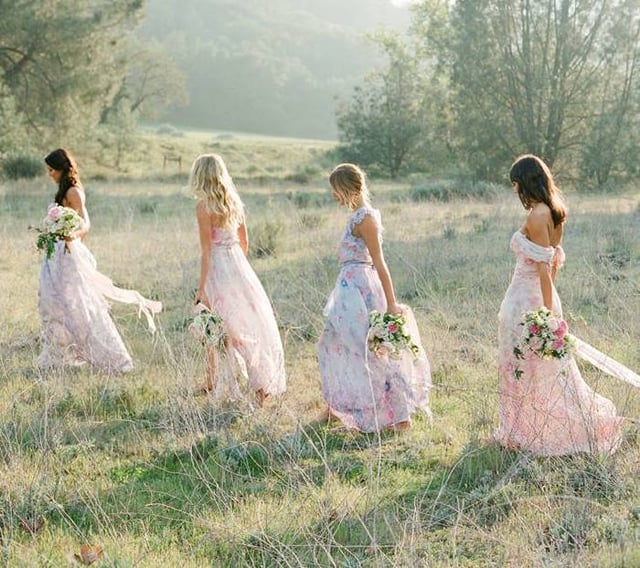 bridesmaids in light floral dresses holding bouquets out in a prairie