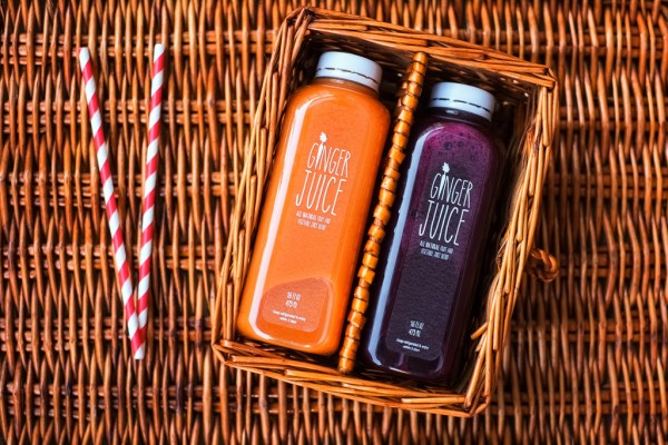 Image of two ginger juice drinks in a brown wicker basket. one is orange and one is purple with two striped straws