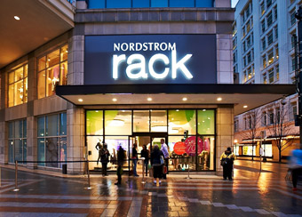 Nordstrom Rack storefront at night. store is 2 stories tall and in a downtown area