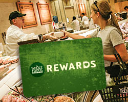 A foreground image of a Whole Foods Market rewards card with someone receiving food at the deli in the background