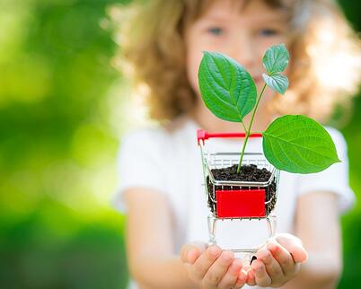 Little girl holding a mini shopping cart in her hands with a plant and soil inside the shopping cart