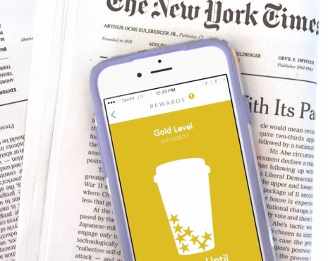 iPhone laying on top of New York Times publication with the screen on the iphone displaying gold level status for Starbucks rewards
