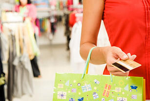 Woman in red dress holding a present-themed shopping bag and a credit card while shopping in a store