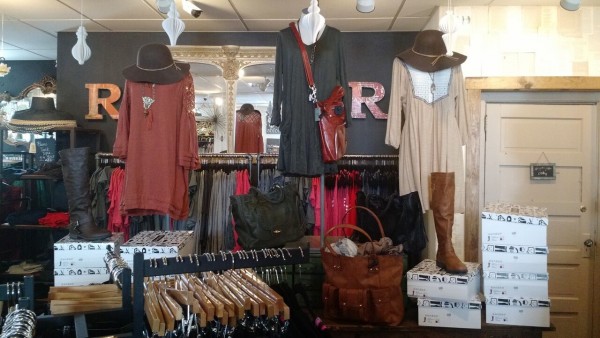 Inside of Rose and Remington store with clothing on display in shades of dark red, gray, and tan