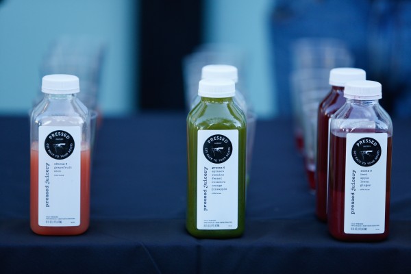 Cold pressed juices on display in rows with sample cups behind them. Two of the juices are not completely filled.Juice colors are pink, green, and purple