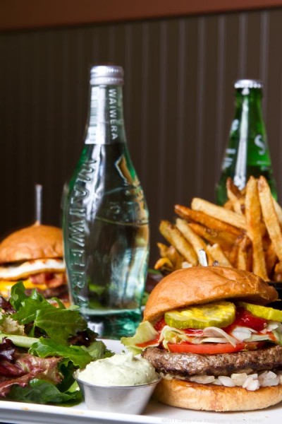 Burgers, fries, and bottled water and sprite on a restaurant table