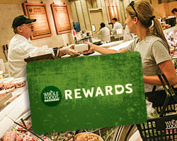 a foreground image of a Whole Foods Market rewards card with someone receiving food at the deli in the background
