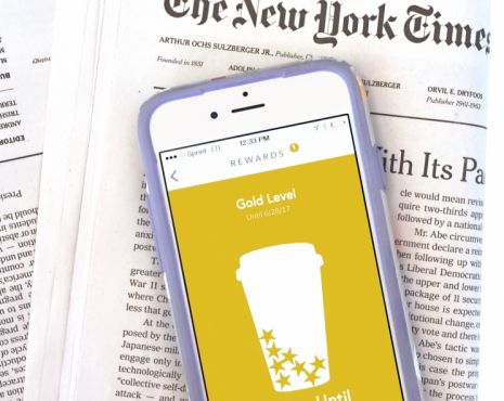 iPhone laying on top of New York Times publication with the screen on the iphone displaying gold level status for starbucks rewards