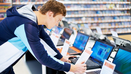 Young male in blue hoodie jacket inside of a store looking at laptop options for purchase