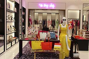 interior of women's fashion store with handbags, clothes, high heels and a mannequin wearing a yellow dress