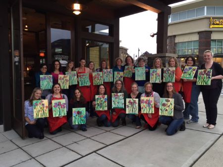 Group of women posing with paintings of flowers. 