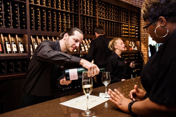 server pouring wine into a glass while behind the bar