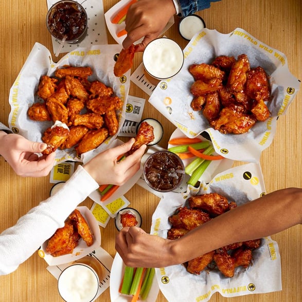 Overhead photo of four hands reaching for wings. 