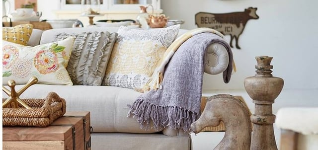 A couch covered in decorative pillows with two large wooden chess pieces in front of it. 