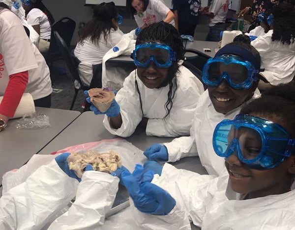 3 young children wearing goggles and lab coats dissecting an animal