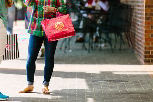 Shopper in red and green flannel hold a bright red shopping bag at a shopping plaza