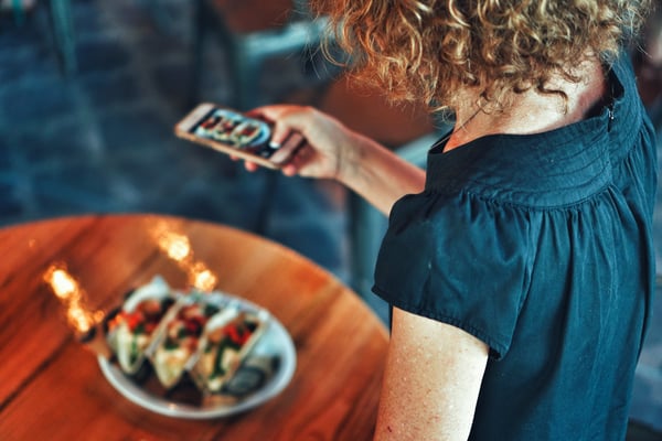 woman taking a photograph of tacos from mobile device