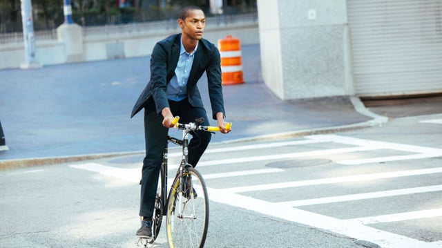 Bicycler in a causal suit riding in a city. 