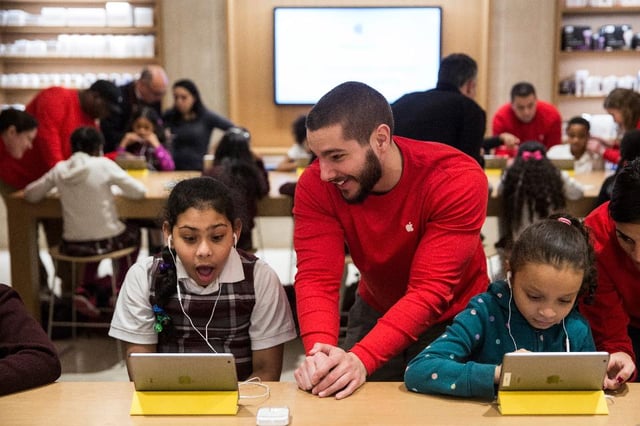 Apple employee showing an iPad to a young girl inside an Apple store. 