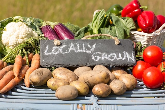 A mix of fresh vegetables outside with a sign that reads, "Locally grown." 