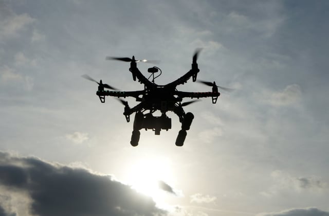 A drone flying with the sun and sky behind it. 