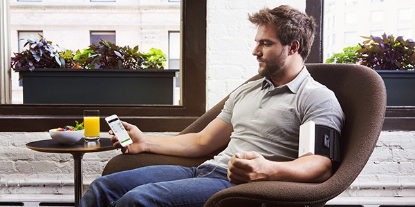 Man in chair using Qardio device on his arm. 