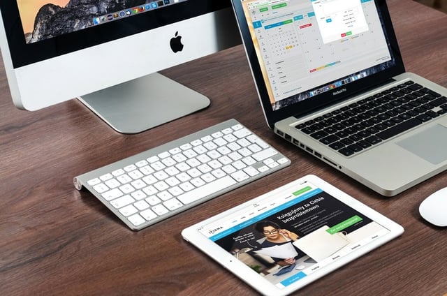 two computers, a keyboard, and ipad on a desk