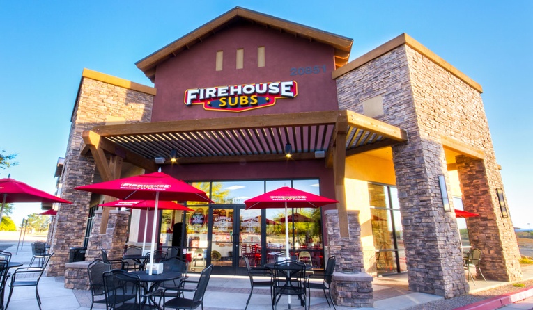 Firehouse Subs storefront with tables and chairs out front. 