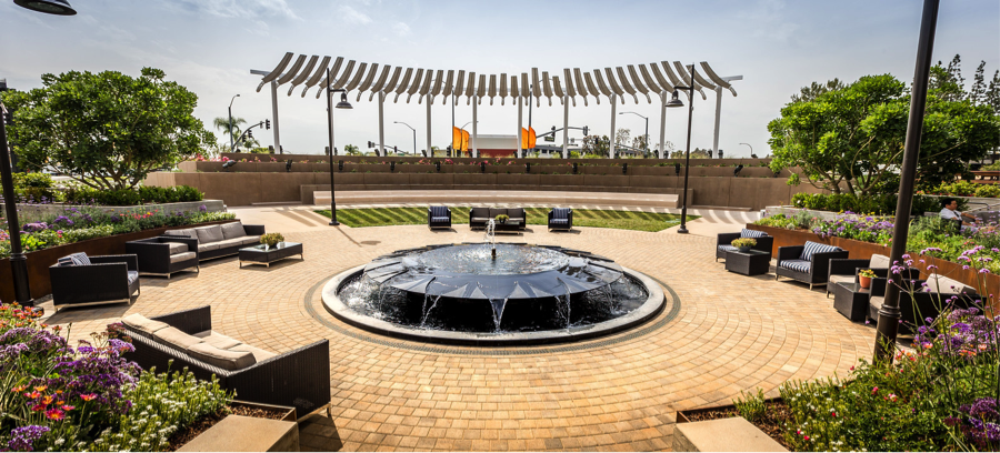 Circular outside seating area surrounded by plants and flowers, with a fountain in the middle.