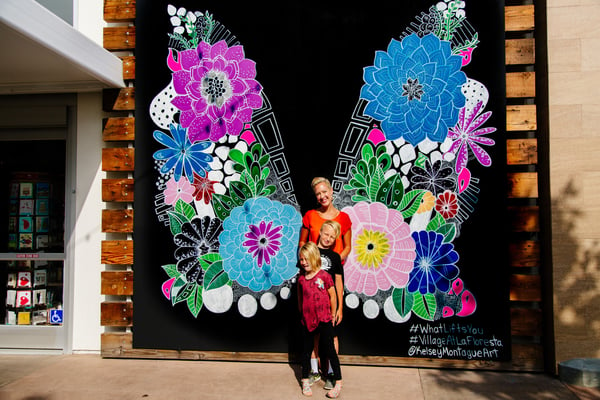 Kelsey Montague posing with her two children in front of a mural. 