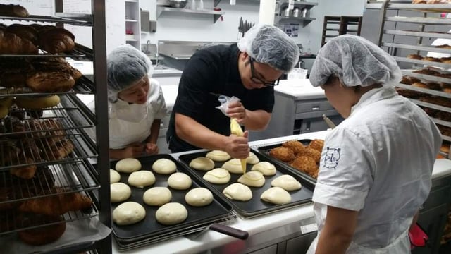 A baker in the kitchen piping icing on dough. 