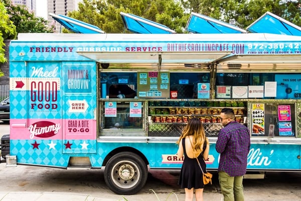 Two customers standing next to a bright blue food truck. 