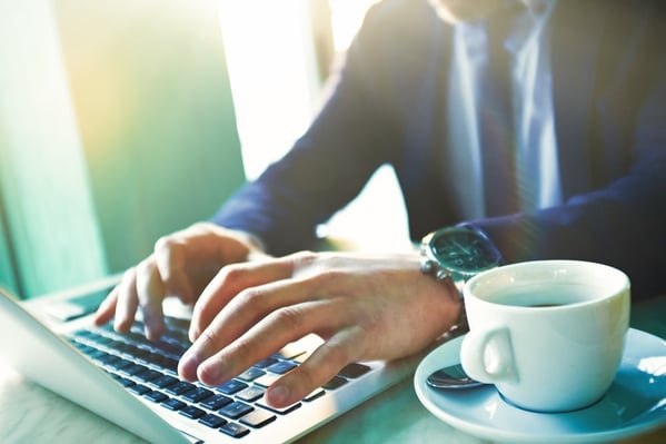 Man using a laptop with a cup of coffee next to him. 