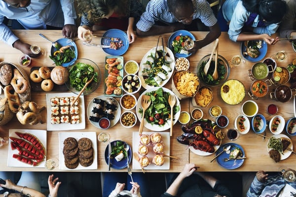 Overhead view of people gathered around a long table covered in plates of food. 