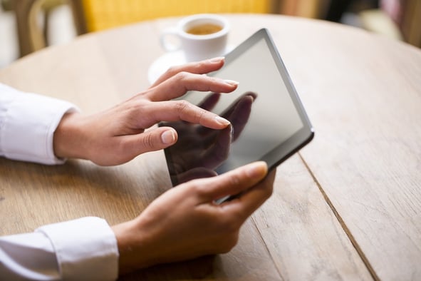 Close-up of a woman using a tablet with a cup of coffee in the background. 