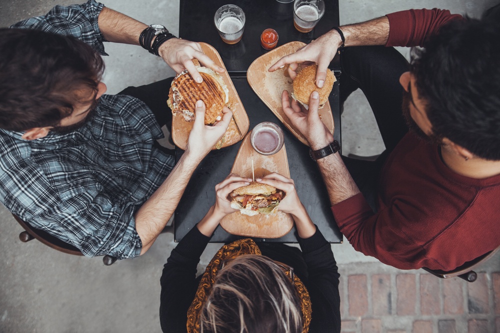 Overhead view of friends at a table, holding sandwiches. 