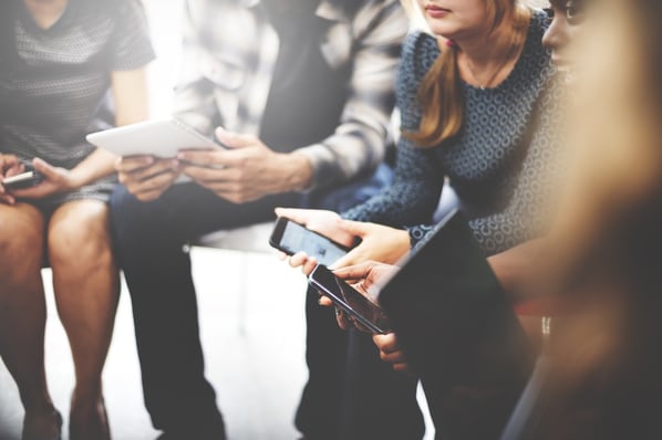 People sitting in a circle while holding various phones and tablets. 