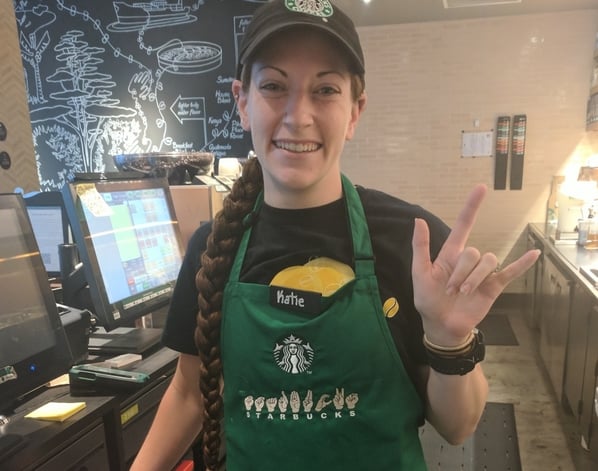 Barista wearing an apron with "Starbucks" spelled out in sign language. 