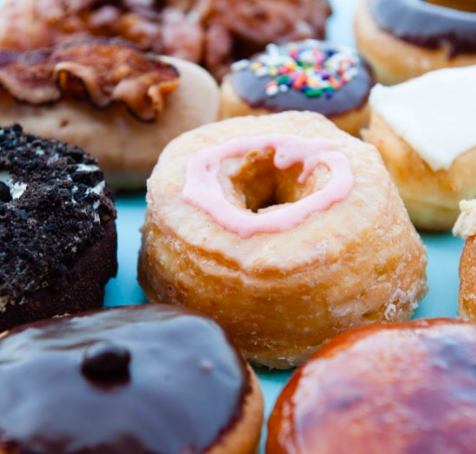 Various donuts, with one with a strip of bacon on top. 