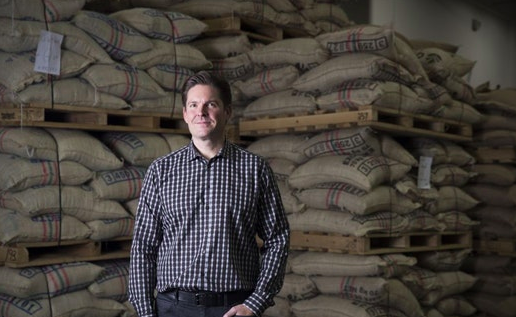 John Puckett posing in front of large burlap bags of coffee beans. 