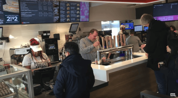 Customers ordering at modern Dunkin' Donuts with coffee on tap. 