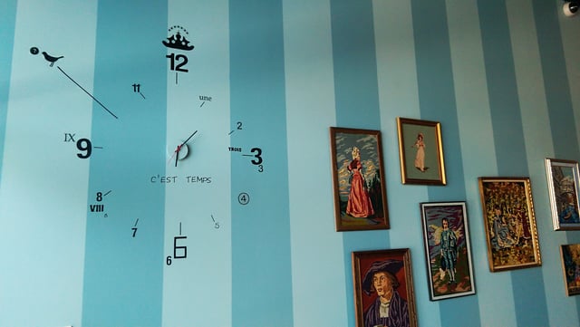 Blue striped wall with a frameless clock and framed paintings inside Amelie's