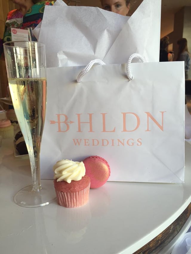 Shopping bag, a pink mini cupcake and macaron, and a glass of champagne on a table.