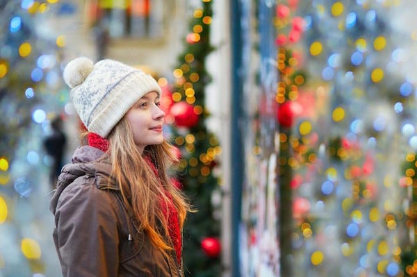 Woman wearing winter clothes, with blurred Christmas decorations behind her. 