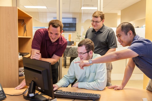 Four interns are laughing at a computer screen. 