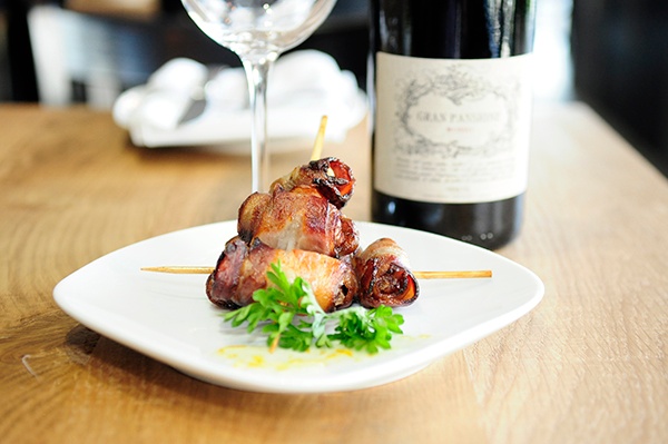 Bacon wrapped dates on a small plate and a bottle of wine next to it. 