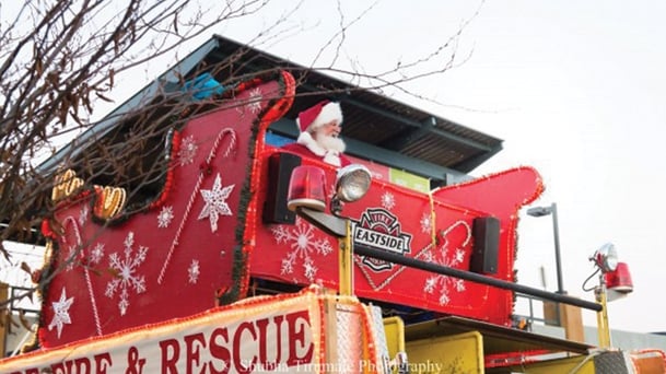 Santa sitting in a sleigh that's sitting atop a fire truck. 